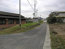 日鉱本幸崎駅跡（写真中央） 国鉄バス「本幸崎」であったバス停は大分バス「神崎中学校」に変更されている。かつては見通しの良い直線であった線路跡も、国道197号のバイパス道路によって視界を絶たれてしまっている。