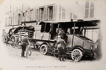 Photo noir et blanc d'un véhicule automobile en tête d'un convoi de fourgons.