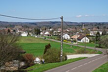 Photo couleur d'une route cheminant à travers champs. En arrière plan : agglomération.