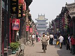 A street lined by traditional houses with red lampions leading to a multi-storied gate.