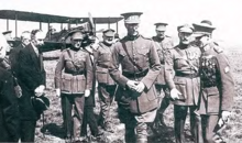 Photographie noir et blanc de divers hommes en uniformes marchant. Un avion se trouve à l'arrière plan.