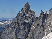 Paroi rocheuse massive dont la crête se détache sur un fond de ciel bleu, quelques plaques de neige recouvrent les rochers