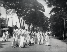 Female students, dressed in white, march down a street.