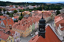 Barevná fotografie s pohled z věže domu přes náměstí a domy vesměs s červenými střechami