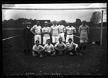 Photo d'équipe sur deux rangs, les joueurs du premier rang étant assis. L'équipe est placée devant l'un des buts.