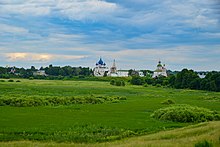 Photographie d'une prairie verte avec une église en arrière-plan.