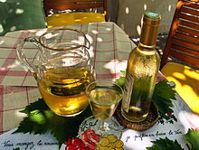 Photographie en couleur illustrant bien la chanson « Ah, le petit vin blanc… ». Une carafe de vin blanc avec un verre plein et une bouteille bouchée sont posés sur des feuilles de vigne, elles-même sur une nappe blanche à carreaux rouges. La bouteille couverte de buée donne une sensation de fraîcheur et le jeu d'ombre et de lumière laisse penser que la scène est située sous une tonnelle,