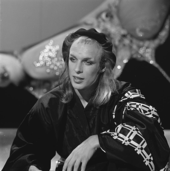 Portrait en noir et blanc de Brian Eno avec des cheveux longs surmontés d'un béret