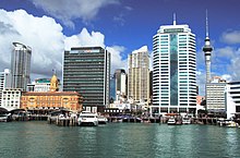 Boats docked in blue-green water. Plate glass skyscrapers rising up in the background.