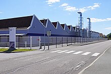 Long bâtiment blanc à toit de sheds.