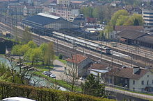 Gare au milieu de la ville sur une voie ferrée avec une verrière surplombant les quais, les voies et un train.