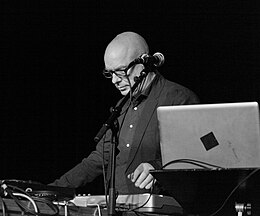 Portrait en noir et blanc de Brian Eno sur scène comme DJ en 2012.