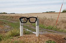 Une sculpture représentant deux poteaux blancs tenant une monture de lunettes noires comme celles de Buddy Holly.